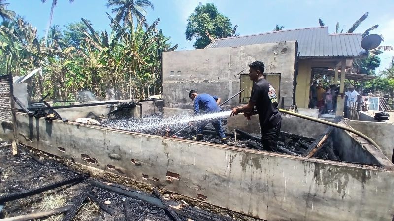 Tim pemadam kebakaran Pos Simpang Mamplam, menyiram puing-puing rumah Afifuddin yang ludes terbakar tadi siang.