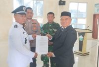 Camat Kota Juang, Saifuddin S.KM M.Kes menyerahkan SK kepada Keuchik Geulanggang Baro, Syafruddin usai prosesi pelantikan di aula Kantor Camat, Sabtu (15/08)